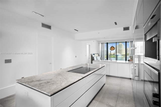 kitchen featuring black electric cooktop, light stone counters, white cabinetry, and an island with sink