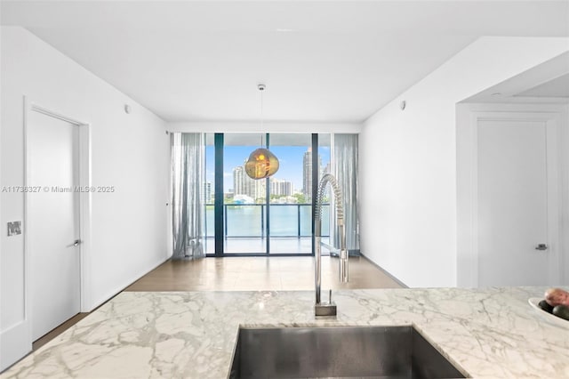 kitchen with light stone countertops, sink, a wall of windows, and decorative light fixtures