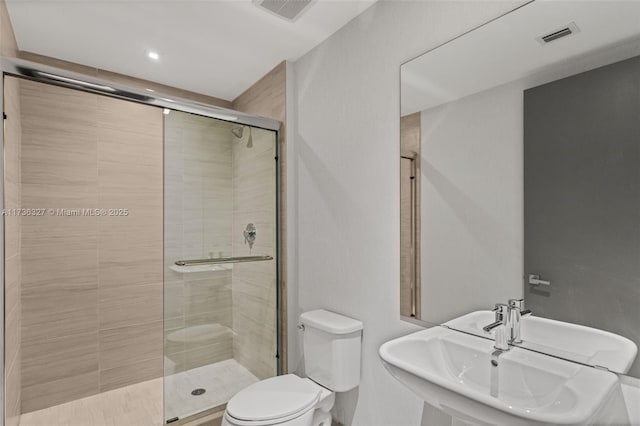 bathroom featuring toilet, a shower with shower door, and sink