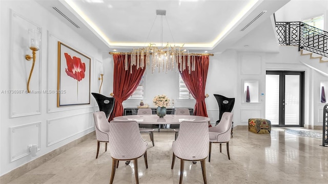 dining area with an inviting chandelier, a tray ceiling, and french doors