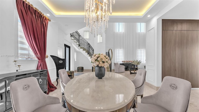 dining area with a towering ceiling, a healthy amount of sunlight, a tray ceiling, and a notable chandelier