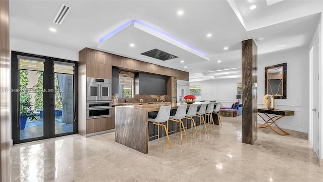 kitchen with french doors, a kitchen breakfast bar, double oven, a large island, and light stone countertops