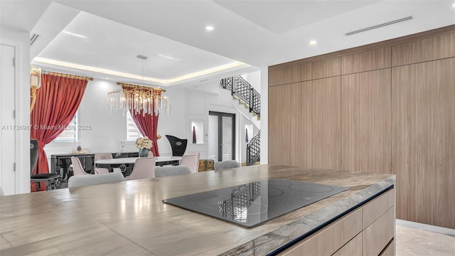 kitchen featuring a raised ceiling, black electric stovetop, and a chandelier