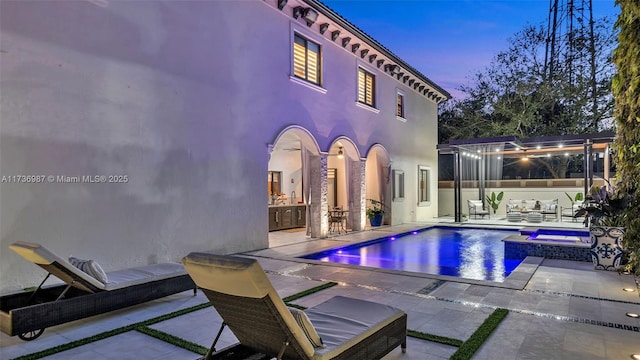 pool at dusk with an in ground hot tub and a patio