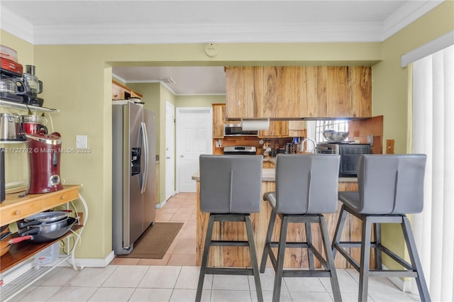 kitchen featuring light tile patterned floors, crown molding, a kitchen breakfast bar, and appliances with stainless steel finishes