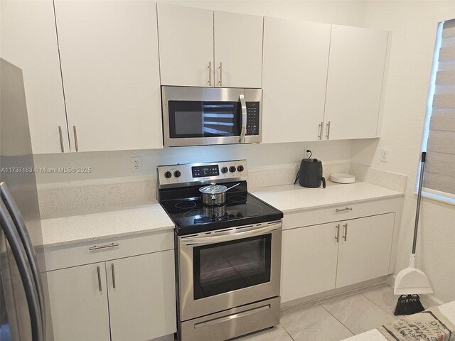 kitchen with sink, light tile patterned floors, appliances with stainless steel finishes, kitchen peninsula, and white cabinets