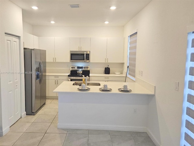 kitchen with light tile patterned flooring, sink, appliances with stainless steel finishes, kitchen peninsula, and white cabinets