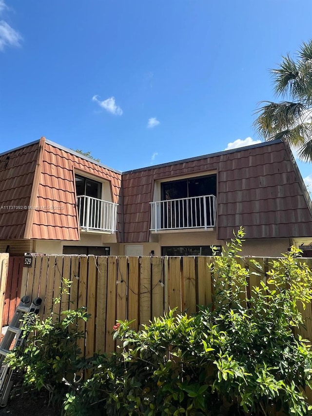 529 Green Springs Pl, West Palm Beach, FL 33409 - view of side of home with a balcony, a tiled roof, mansard roof, fence, and stucco siding