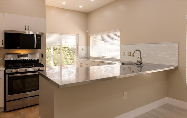 kitchen with sink, white cabinets, backsplash, kitchen peninsula, and stainless steel appliances