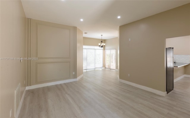 unfurnished room with a chandelier and light wood-type flooring