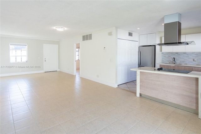 interior space with sink, white cabinetry, tasteful backsplash, stainless steel refrigerator, and island exhaust hood