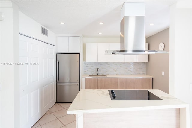 kitchen featuring sink, white cabinetry, black electric cooktop, stainless steel fridge, and island exhaust hood