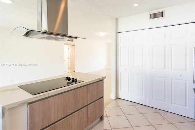 kitchen with island exhaust hood, light stone countertops, light tile patterned floors, and black electric cooktop