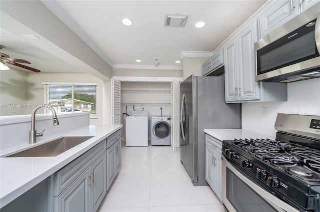 kitchen featuring washing machine and clothes dryer, sink, crown molding, gray cabinets, and stainless steel appliances