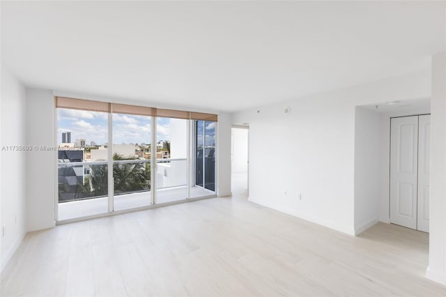 spare room with a wall of windows and light hardwood / wood-style floors