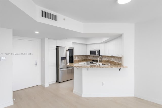 kitchen with stainless steel appliances, light stone counters, white cabinets, decorative backsplash, and kitchen peninsula