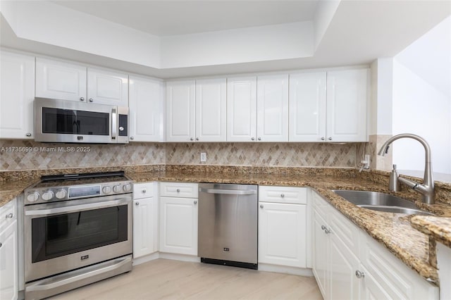 kitchen featuring appliances with stainless steel finishes, tasteful backsplash, white cabinetry, sink, and dark stone countertops