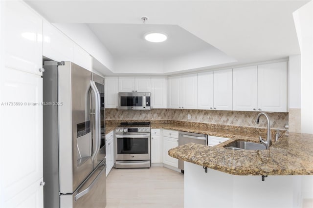 kitchen with sink, appliances with stainless steel finishes, kitchen peninsula, white cabinets, and dark stone counters