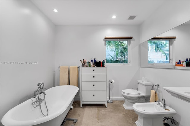 bathroom with a washtub, toilet, and a bidet