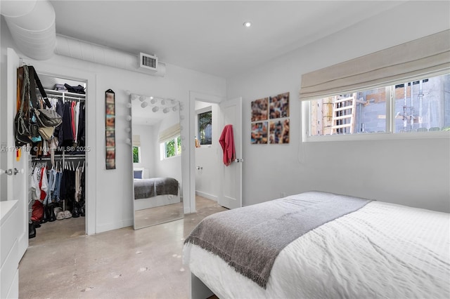 bedroom with a walk in closet, concrete flooring, and a closet