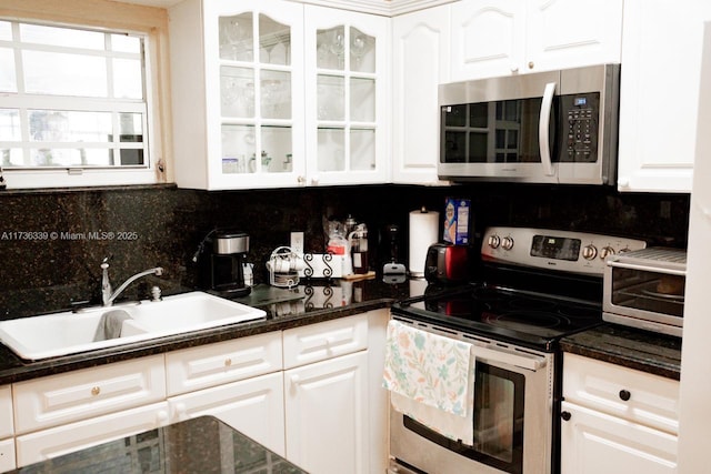 kitchen featuring sink, white cabinetry, dark stone countertops, stainless steel appliances, and backsplash