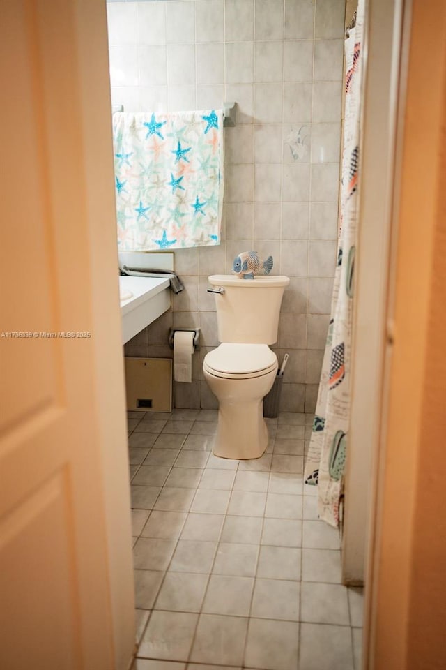 bathroom with toilet, tile patterned flooring, and tile walls