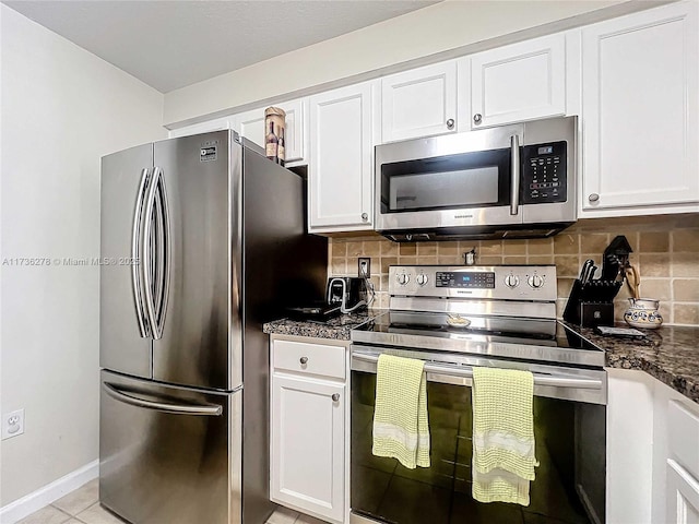 kitchen with light tile patterned floors, dark stone countertops, white cabinetry, stainless steel appliances, and decorative backsplash