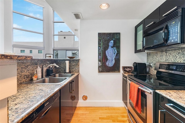 kitchen featuring sink, light hardwood / wood-style flooring, light stone counters, black appliances, and decorative backsplash