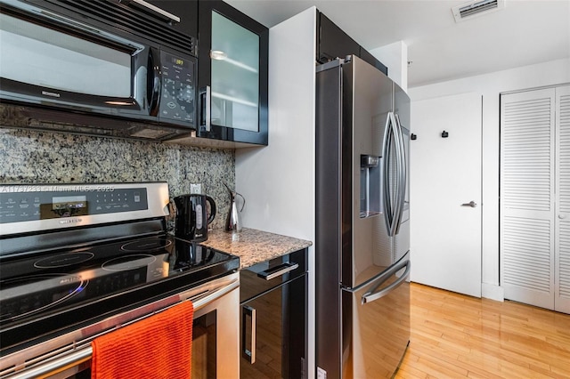 kitchen with appliances with stainless steel finishes, light stone countertops, light hardwood / wood-style floors, and backsplash