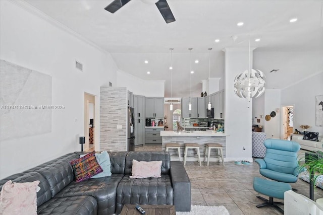 living room featuring light tile patterned floors, crown molding, ceiling fan with notable chandelier, and high vaulted ceiling