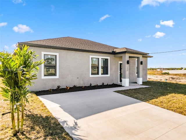 view of front of property featuring a patio area, roof with shingles, a front yard, and stucco siding