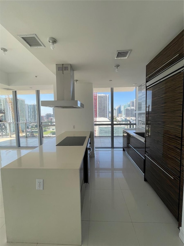 kitchen featuring island range hood, a center island, light tile patterned floors, a wall of windows, and black electric stovetop