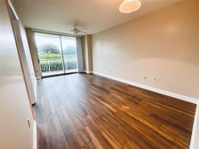 spare room with dark wood-type flooring, a wall of windows, and ceiling fan