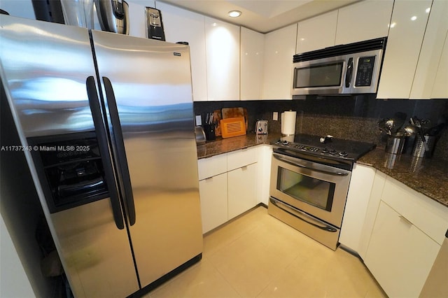 kitchen with light tile patterned floors, appliances with stainless steel finishes, tasteful backsplash, white cabinets, and dark stone counters