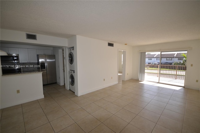 interior space featuring stacked washer and dryer, light tile patterned floors, visible vents, and a textured ceiling