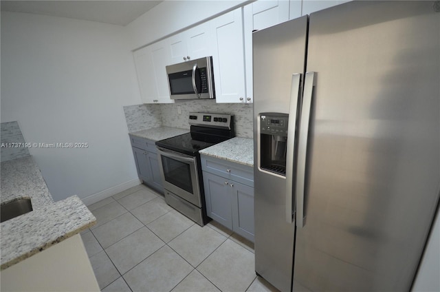 kitchen featuring decorative backsplash, light stone counters, stainless steel appliances, white cabinetry, and light tile patterned flooring