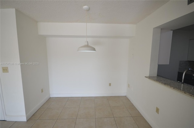 unfurnished dining area featuring a textured ceiling, light tile patterned floors, a sink, and baseboards