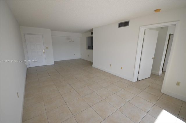 unfurnished room featuring a textured ceiling, light tile patterned floors, visible vents, and baseboards