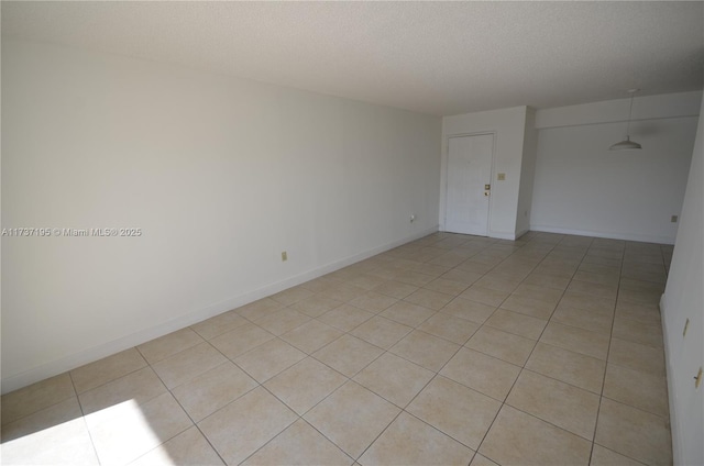 empty room with a textured ceiling, light tile patterned floors, and baseboards