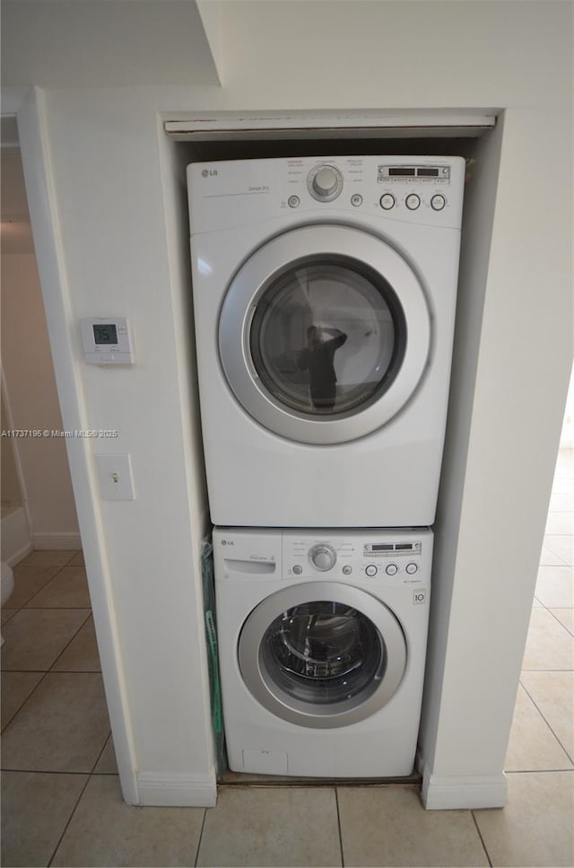 clothes washing area featuring light tile patterned floors, stacked washer and clothes dryer, and baseboards