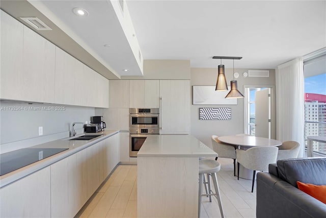 kitchen with sink, a breakfast bar area, double oven, hanging light fixtures, and a center island