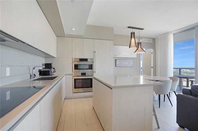 kitchen with sink, double oven, a kitchen island, pendant lighting, and a wall of windows