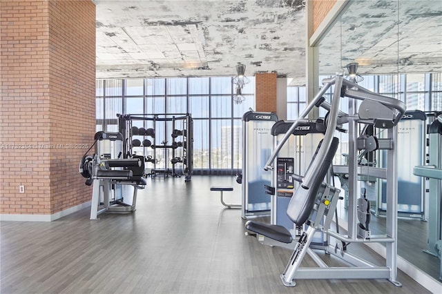 exercise room with expansive windows, wood-type flooring, and brick wall