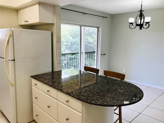 kitchen featuring pendant lighting, a breakfast bar area, white cabinetry, white refrigerator, and dark stone counters