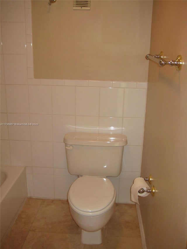 bathroom featuring tile patterned floors, toilet, a bathtub, and tile walls