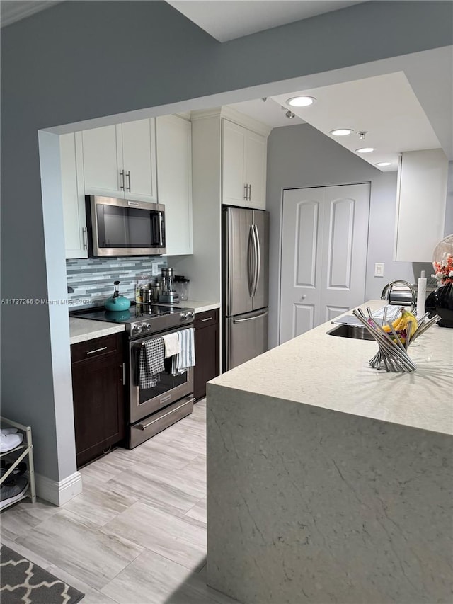 kitchen featuring sink, white cabinetry, dark brown cabinets, appliances with stainless steel finishes, and backsplash