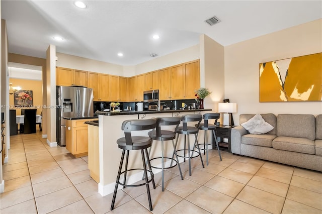 kitchen with light brown cabinetry, light tile patterned floors, appliances with stainless steel finishes, a kitchen breakfast bar, and kitchen peninsula