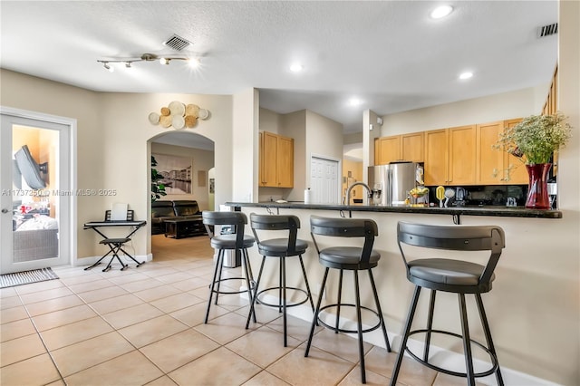 kitchen featuring a breakfast bar area, light tile patterned floors, kitchen peninsula, stainless steel refrigerator with ice dispenser, and a textured ceiling