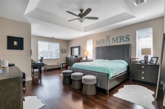 bedroom with a raised ceiling, ceiling fan, dark hardwood / wood-style floors, and multiple windows