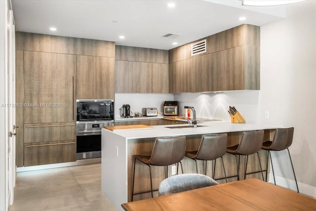 kitchen featuring sink, a kitchen breakfast bar, black microwave, kitchen peninsula, and stainless steel oven